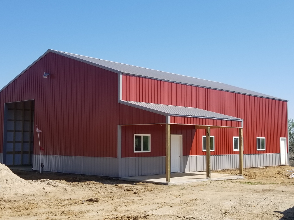 Red steel barndominium with gray wainscot, covered front porch, and oversized shop door in Kansas